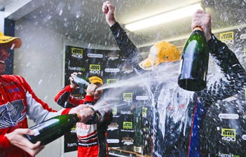 thumb Garth Tander gives Shane van Gisbergen a spray on the Hamilton podium – van Gisbergen's first win in the V8 Supercars Championship